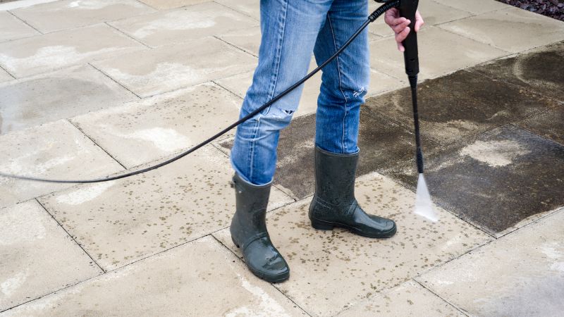 A person wearing waterproof boots pressure washing a patio. This shows how hardscaping maintenance is an important part of a 'how to spring clean your garden' checklist.